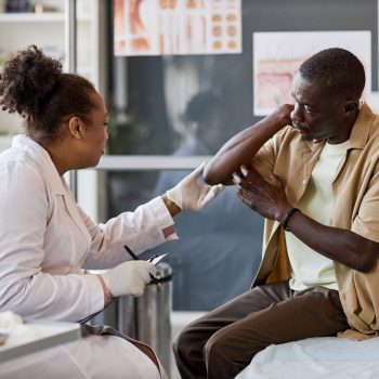 Side view portrait of African American woman as female dermatologist consulting patient in clinic and examining skin